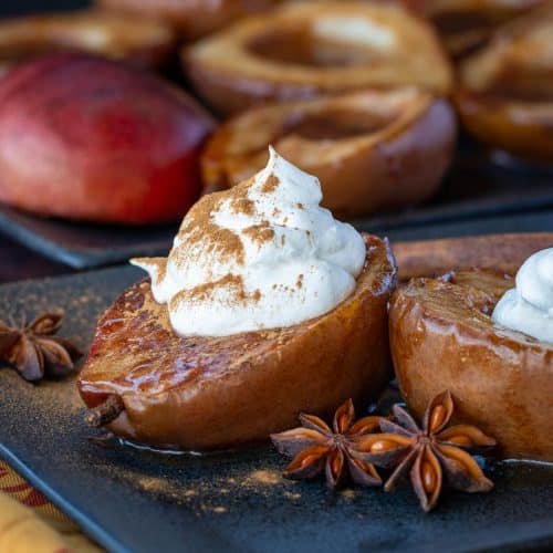 Asian Spiced roasted pears on a black plate topped with coconut whipped topping.