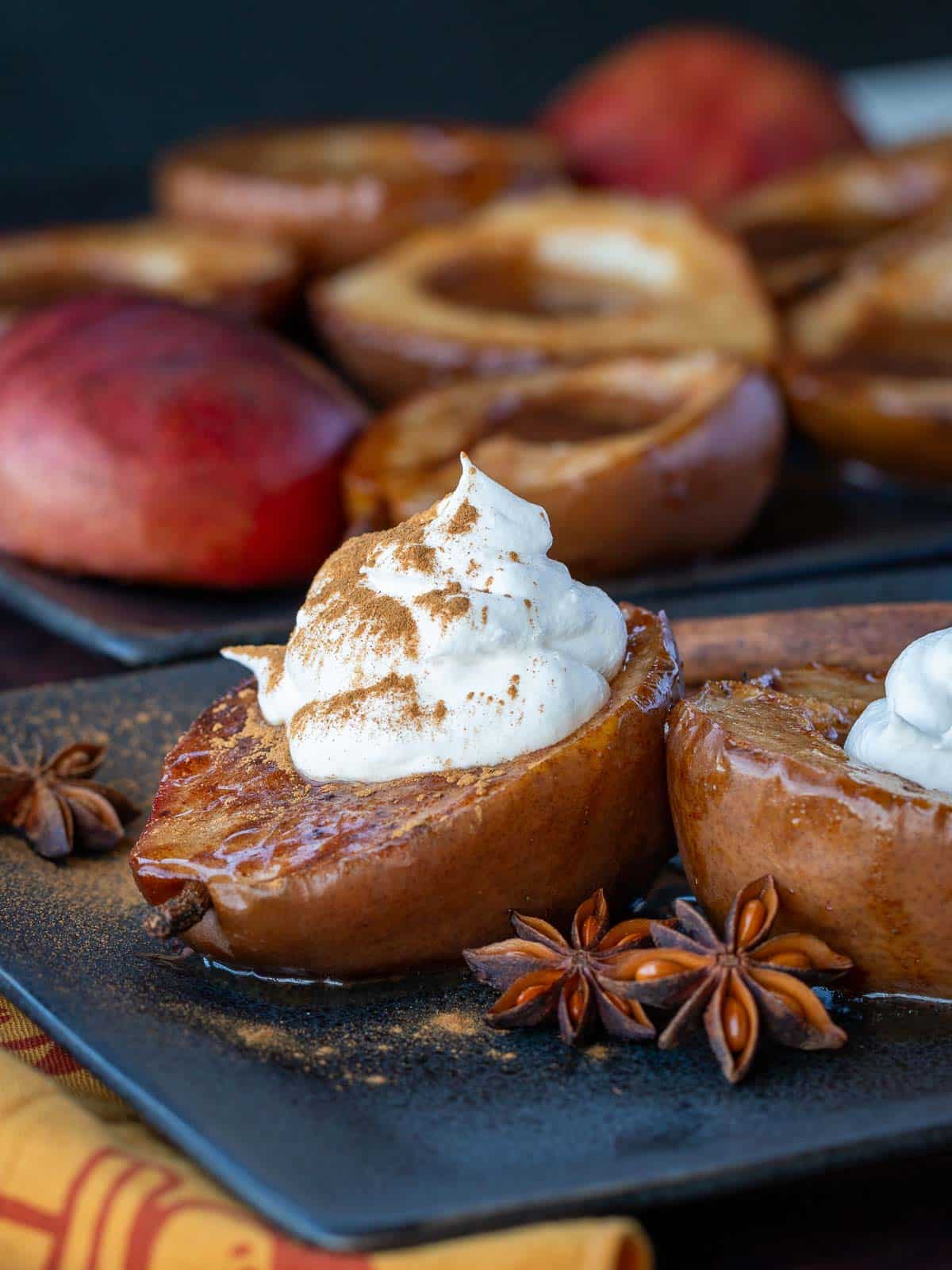 Baked pear dessert topped with homemade coconut whipped cream on a black plate garnished with dried star anise and cinnamon twills. 