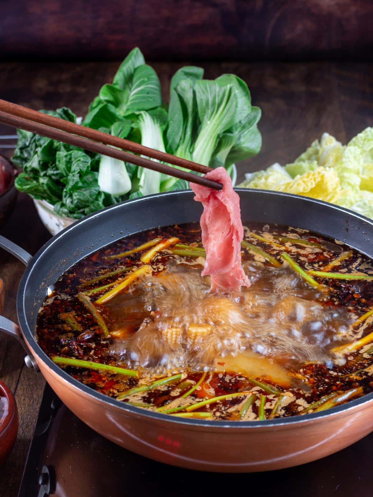 Dipping thin beef slice into boiling Sichuan hot pot. 