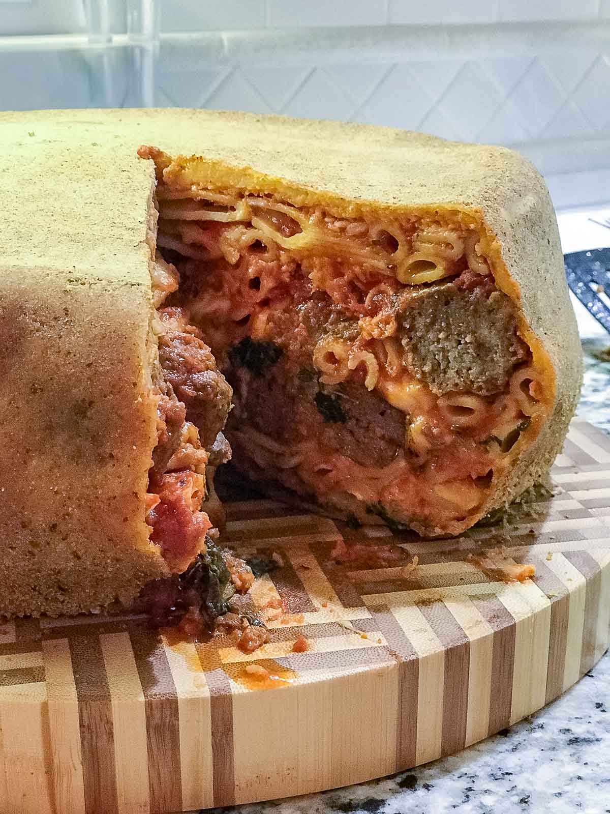 Timpano Pasta Dome cut into showing all the layers of pasta and meatball, cheese and more.