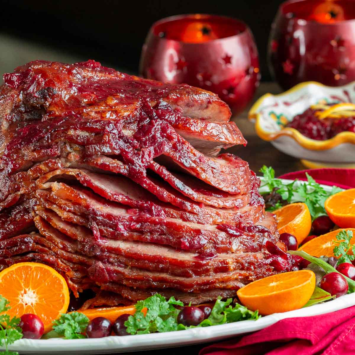 Ham with a festive cranberry glaze served on a decorated Christmas dish. 