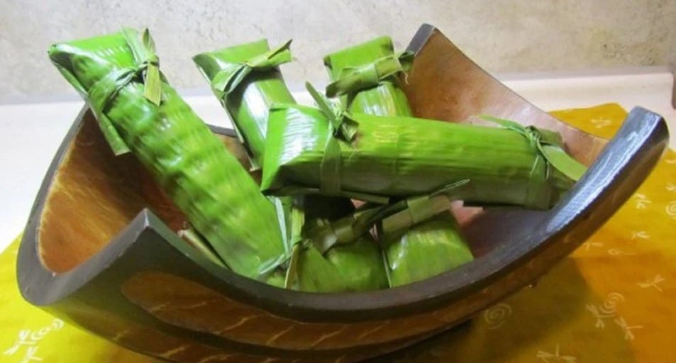 Banana leaf wrapped coconut fish ready to be steamed or grilled in a wooden bowl. 