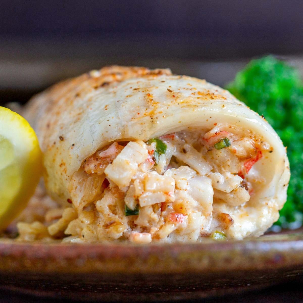 Crab stuffed whitefish on a brown plate with lemon slices. 