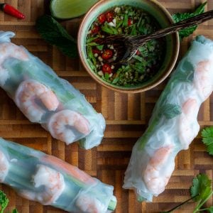 Three summer rolls on a wooden blackboard with a small bowl of dipping sauce.