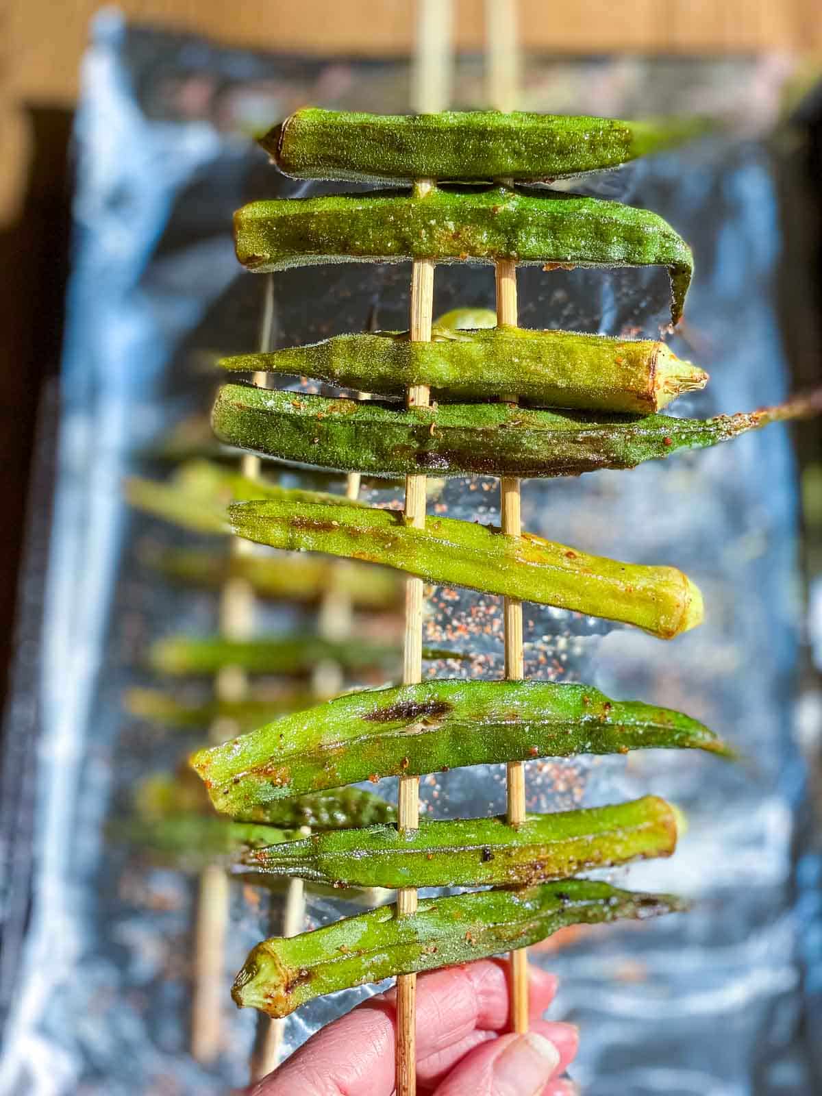 Cooked doubled skewed okra being held by the sticks.
