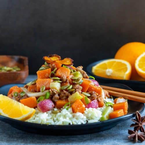 Orange ginger sweet potato stir fry with sausage on a black Chinese plate.