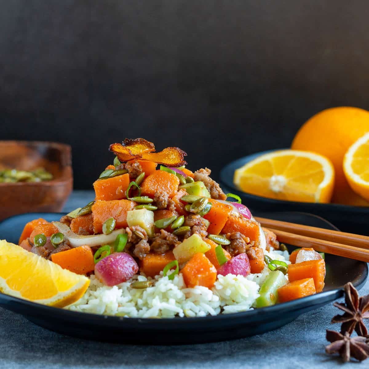 Orange ginger sweet potato stir fry with sausage on a black Chinese plate.