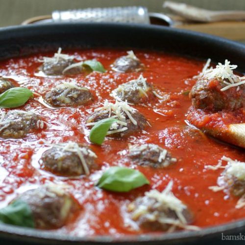 Meatballs in Grandma's sauce in a large skillet cooking.