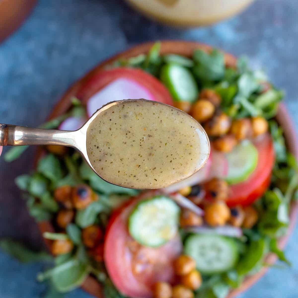 A spoonful of creamy emulsified vinaigrette held over a salad bowl. 