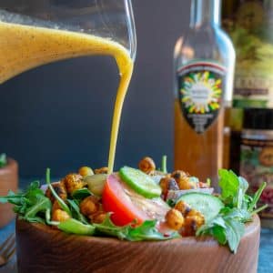 Pouring lemon white balsamic vinaigrette over a tossed garden salad.