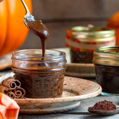 Pumpkin spice coffee sauce in glass jars with a spoon pour with spices, prunes and coffee around the jar.