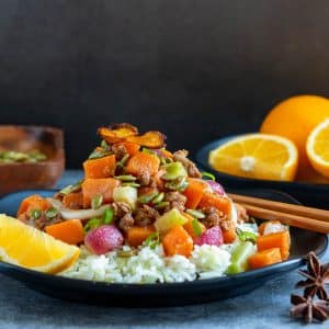 Orange ginger sweet potato stir fry with sausage served over rice on a black plate.