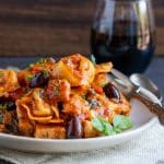 Chicken cacciatore pasta on a white plate with a glass of red wine.