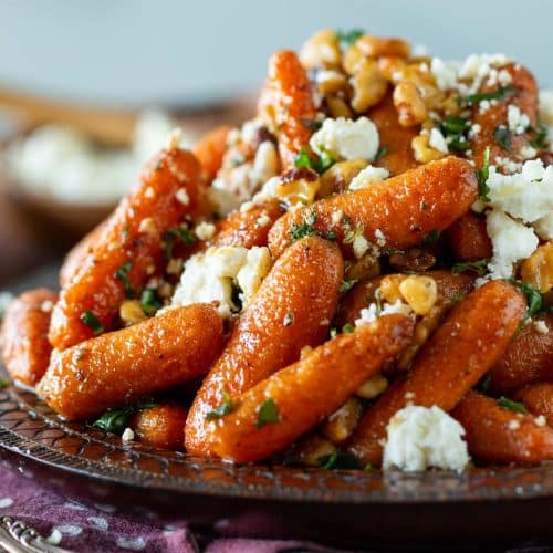 Moroccan spiced air fryer baby carrots topped with feta on a wooden plate.