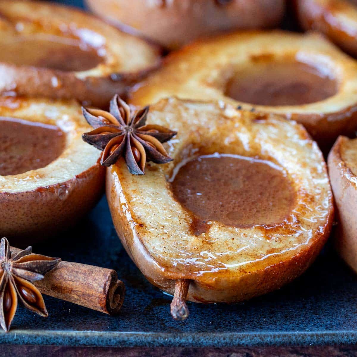 Asian spiced roasted pears on a black plate garnished with star anise and cinnamon twills.