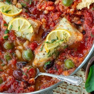 Mediterranean baked cod fish with a fresh tomato, olive, caper and white bean sauce in a skillet.