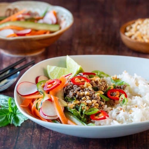 Thai style ground beef bowls topped with Asian carrot slaw in a white bowl.