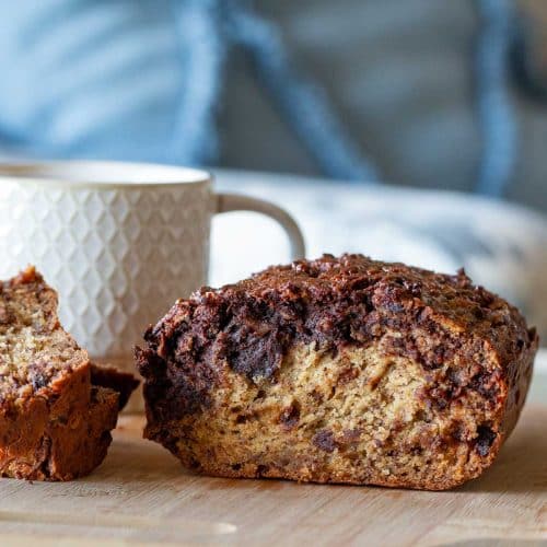 Loaf of Eggless Marbled Chocolate Peanut Butter Banana bread on a cutting board with a cup of coffee.